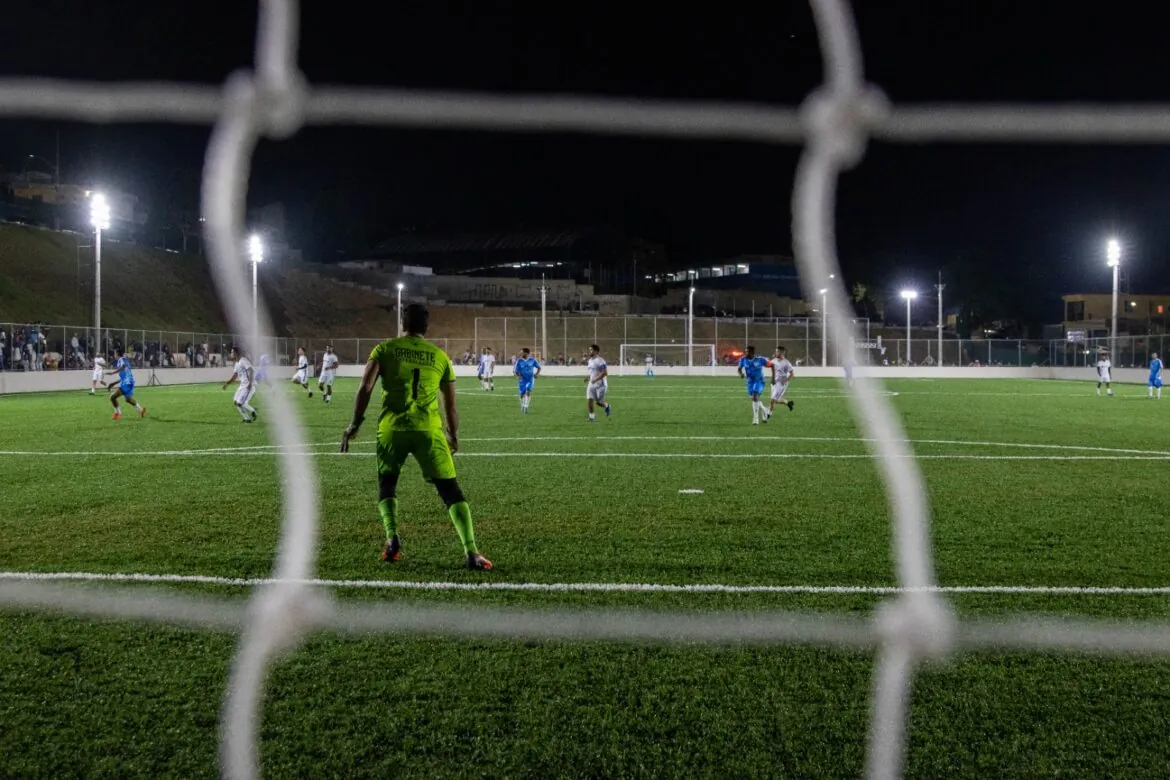 Partida noturna em campo esportivo iluminado, em uso real anos após a entrega