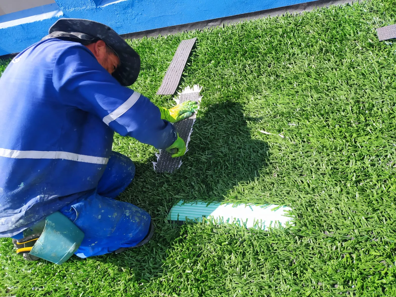 Profissional instalando grama sintética manualmente, com atenção ao detalhe